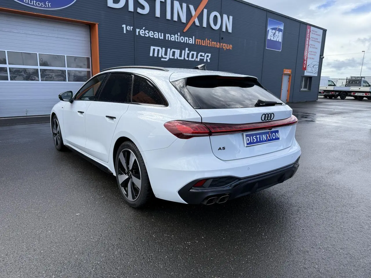 Audi A5 Avant blanc glacier métallisé vue 3/4 arrière droit avec jantes noires et feux arrière LED connectés.