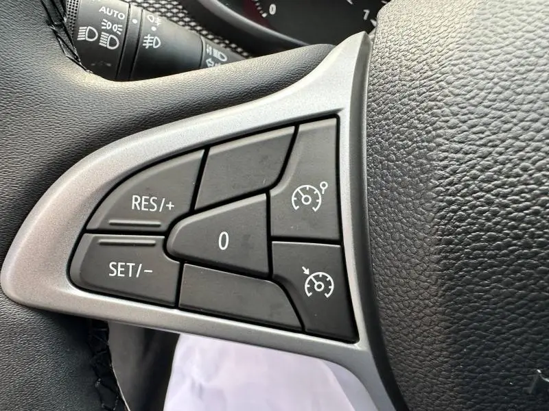 Gros plan sur les commandes de régulateur de vitesse au volant noir de la Dacia Sandero blanche 2025 Stepway Expression