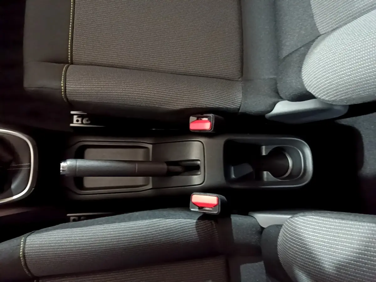 Vue plongeante sur la console centrale noire et les sièges tissu gris avec coutures jaunes de la Citroën C3 blanche 2023.