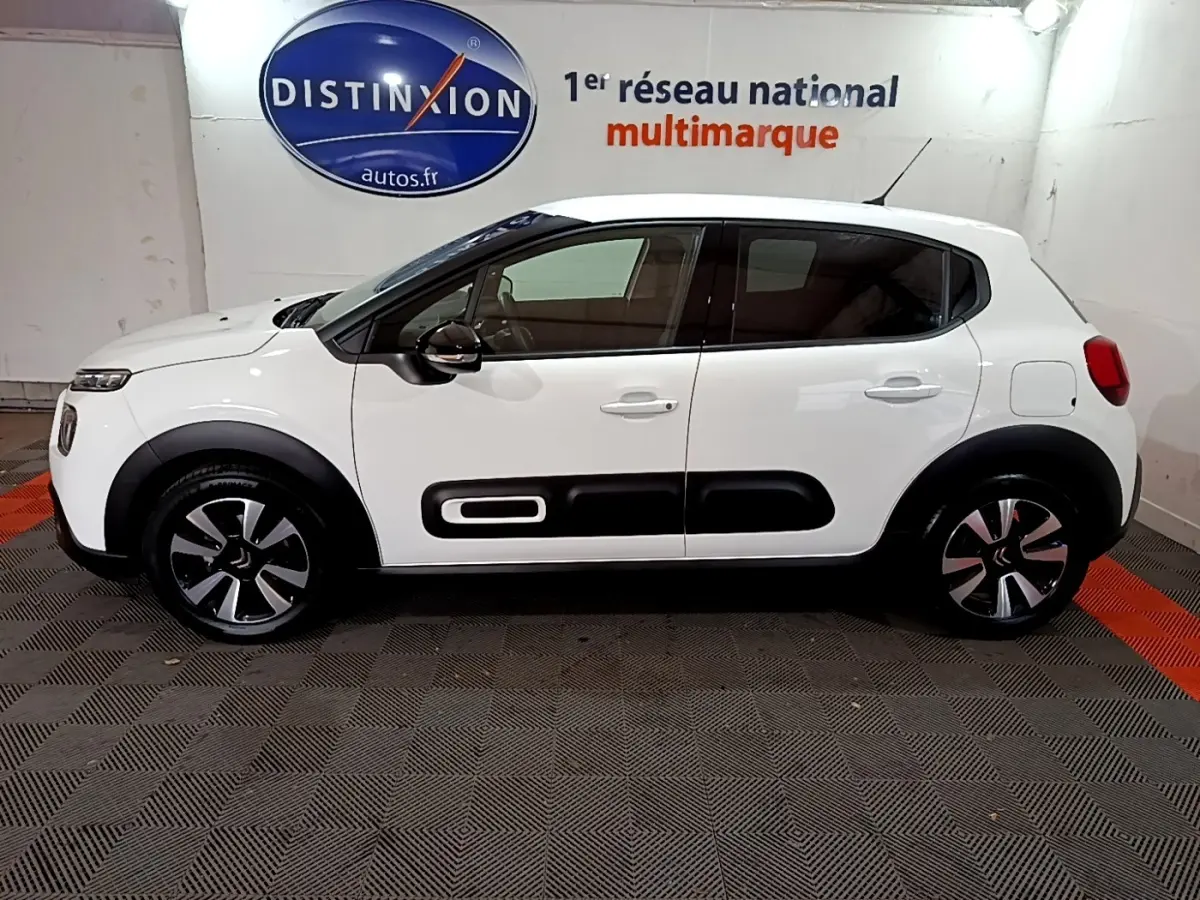 Profil côté gauche d'une Citroën C3 blanche 2023 avec protections latérales noires et jantes stylisées.