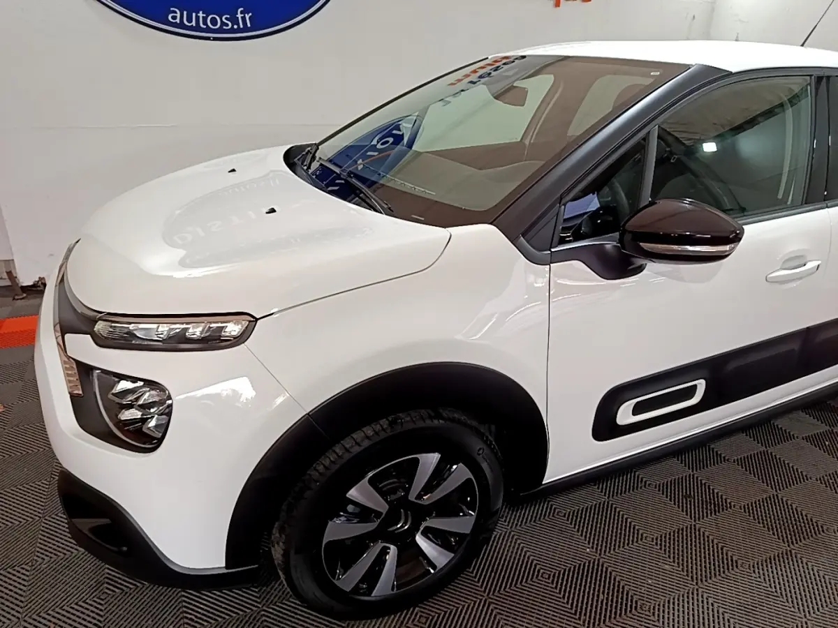 Vue 3/4 avant droit d'une Citroën C3 blanche avec rétroviseurs noirs et protections latérales caractéristiques.