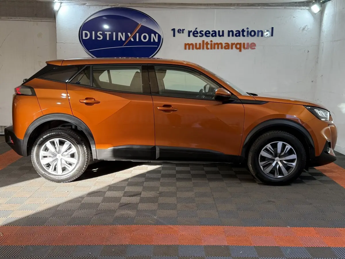 Vue de profil côté gauche d’un Peugeot 2008 orange 2022 avec jantes alliage et protections noires sur les bas de caisse.