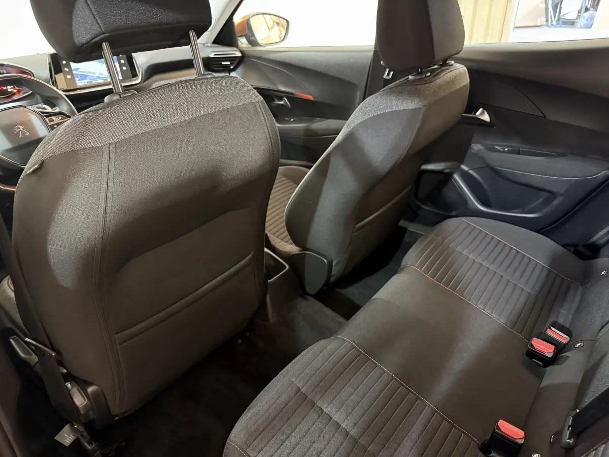Vue intérieure arrière de la Peugeot 2008 2022, sièges tissu noirs avec surpiqûres rouges, tableau de bord et volant visibles.