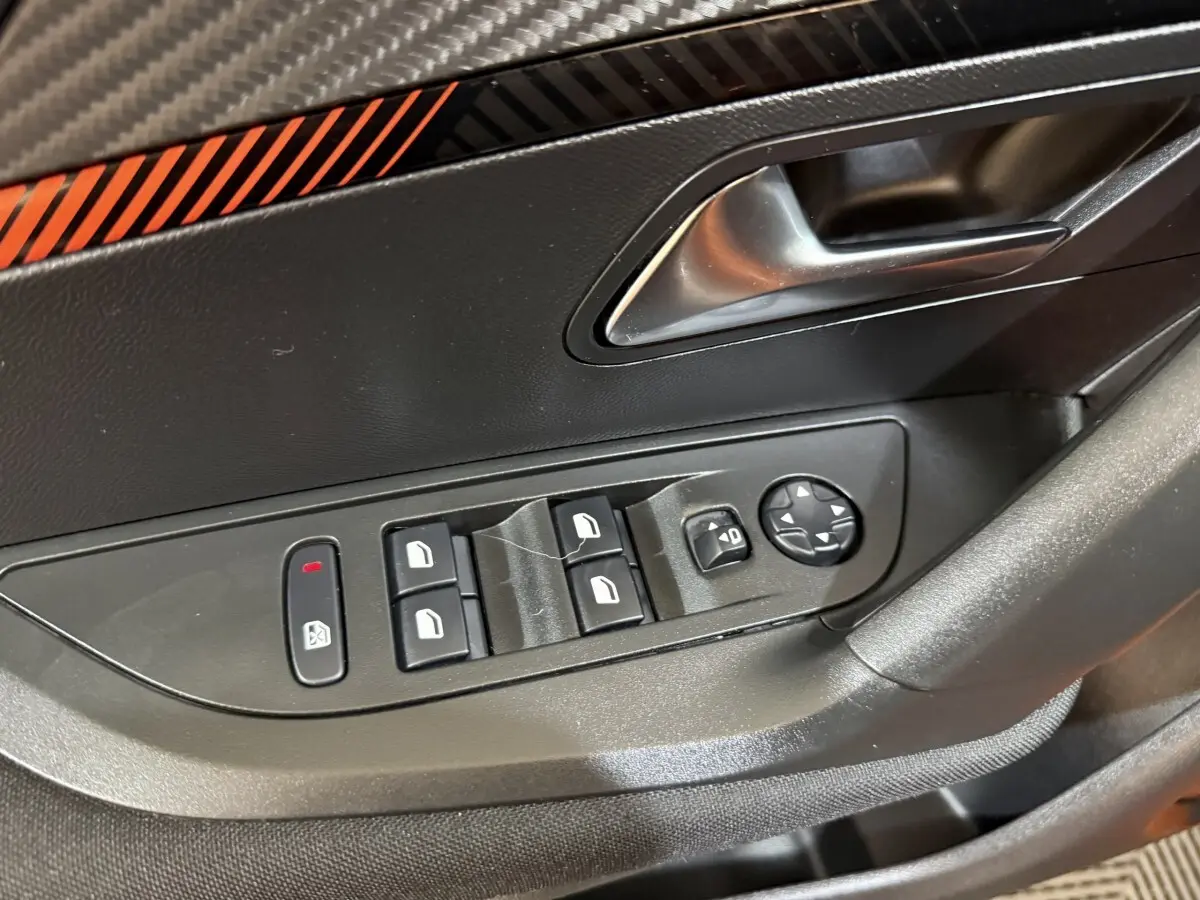 Gros plan sur la commande des vitres et rétroviseurs côté gauche d’une Peugeot 2008 orange, intérieur noir.