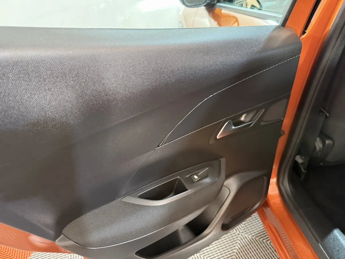 Vue intérieure côté gauche de la porte arrière orange du Peugeot 2008 avec poignée et commande de vitre électrique.