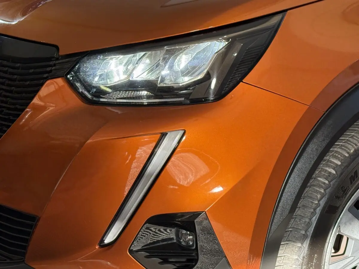 Gros plan sur l'avant droit orange du Peugeot 2008 2022, mettant en valeur le phare LED et le feu antibrouillard.