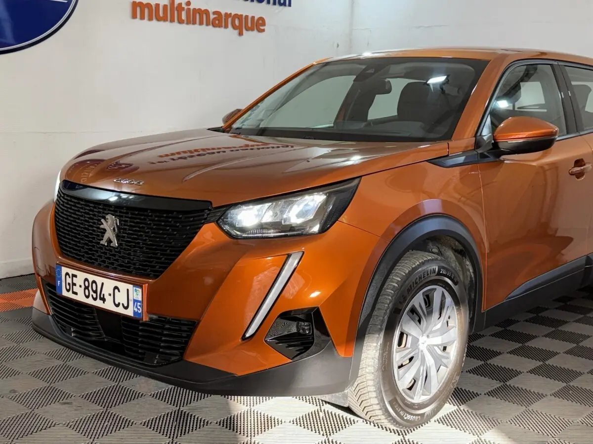 Vue 3/4 avant droit d’un Peugeot 2008 orange 2022 avec calandre noire et phares LED allumés.