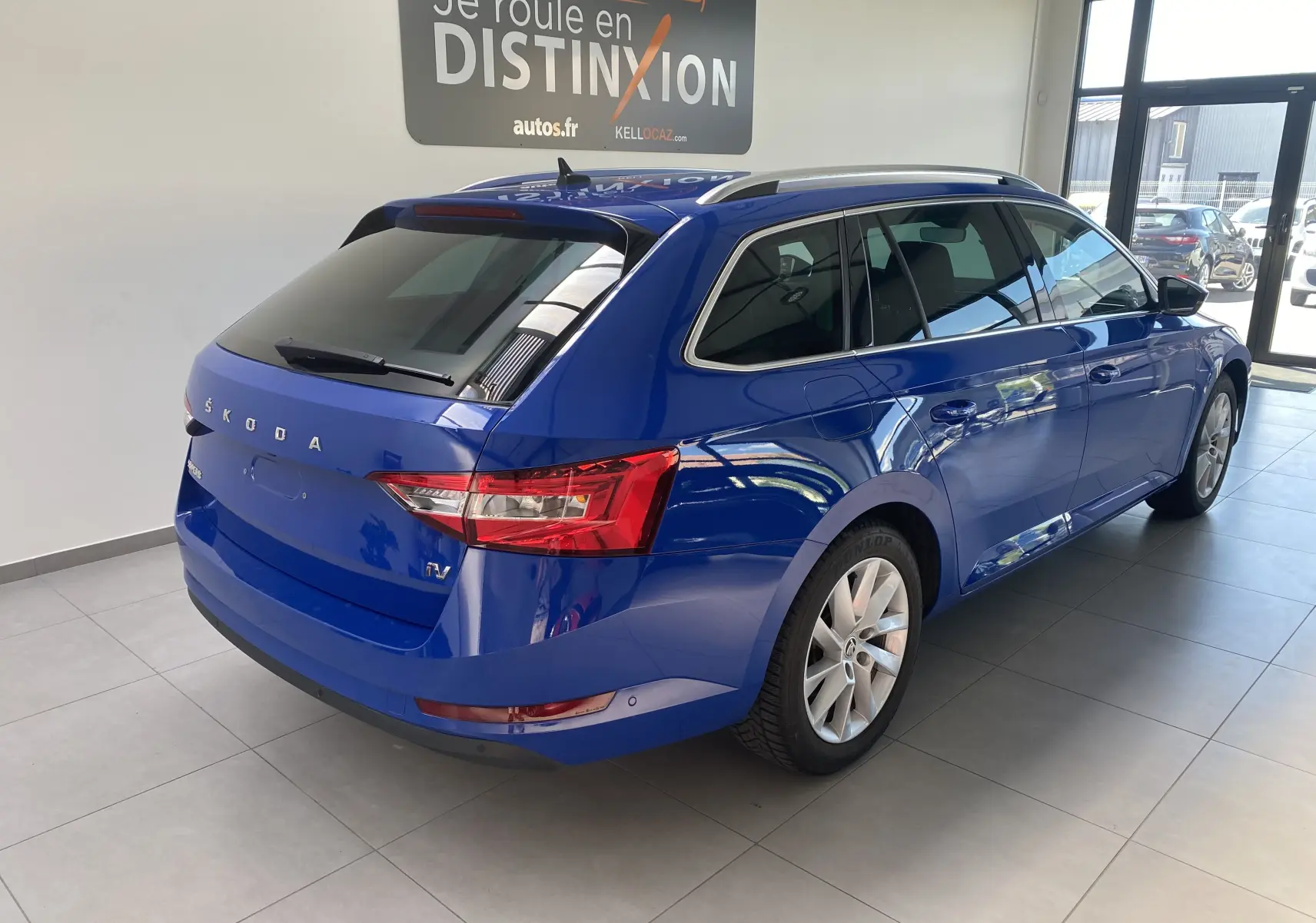 Vue 3/4 arrière droite d'une Skoda Superb Combi IV bleu énergie, break hybride rechargeable en showroom lumineux.