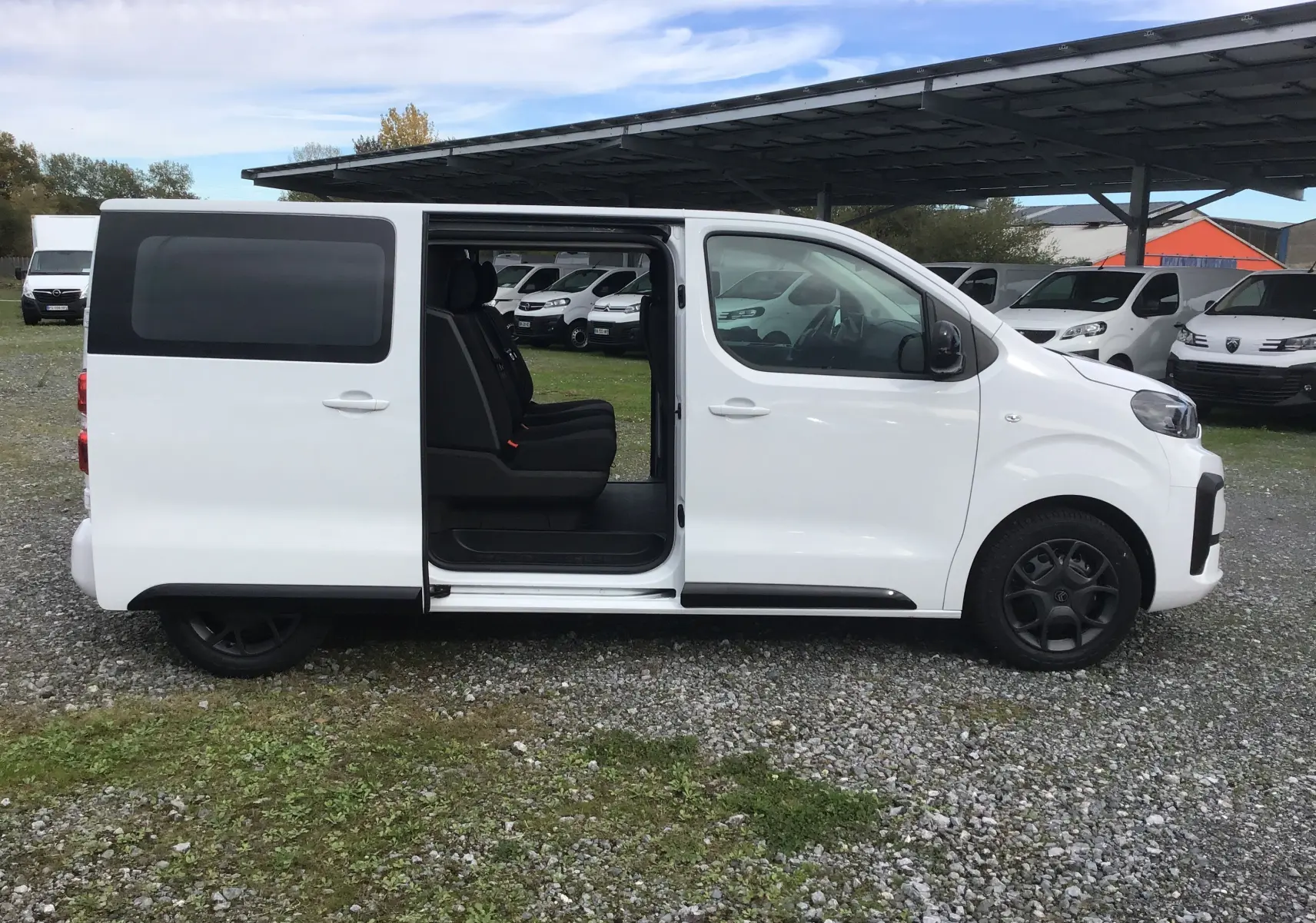 Vue de profil côté droit d'un Citroën Jumpy blanc avec porte coulissante ouverte révélant les sièges arrière noirs.