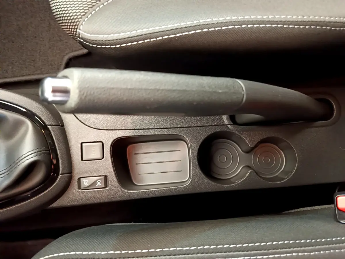 Vue rapprochée de la console centrale noire avec frein à main manuel et porte-gobelets de la Renault Clio Business gris clair.