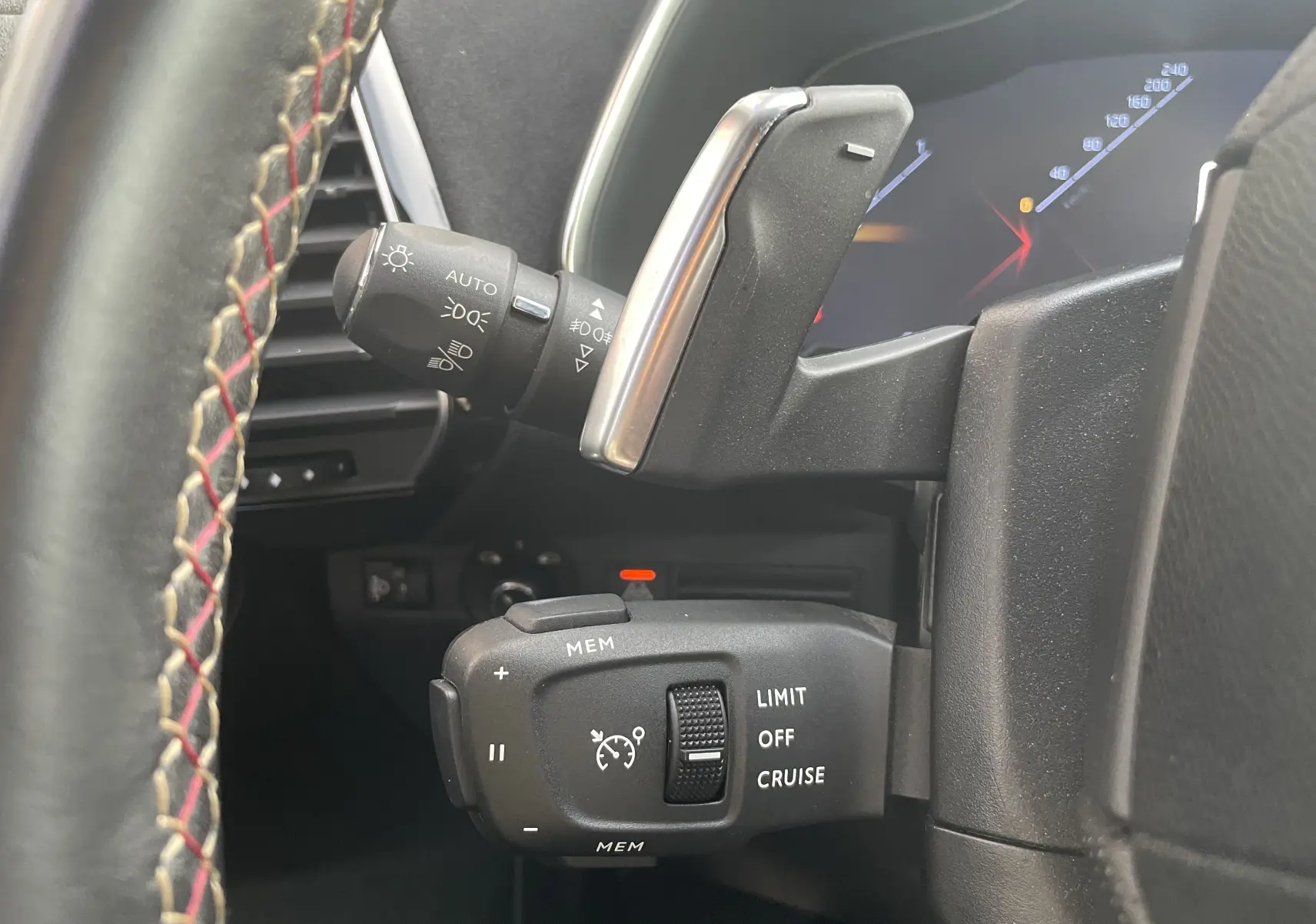 Gros plan sur les commandes au volant du DS7 gris, mettant en valeur le régulateur de vitesse et la manette des phares.