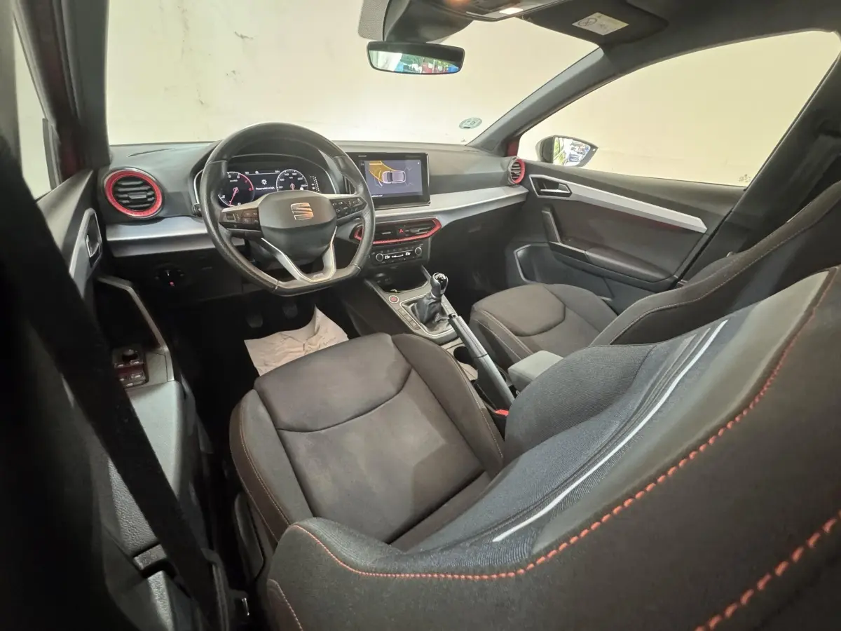 Intérieur de la SEAT IBIZA 1.0 TSI 110 FR vu côté conducteur, sièges noirs avec surpiqûres rouges et volant multifonctions.