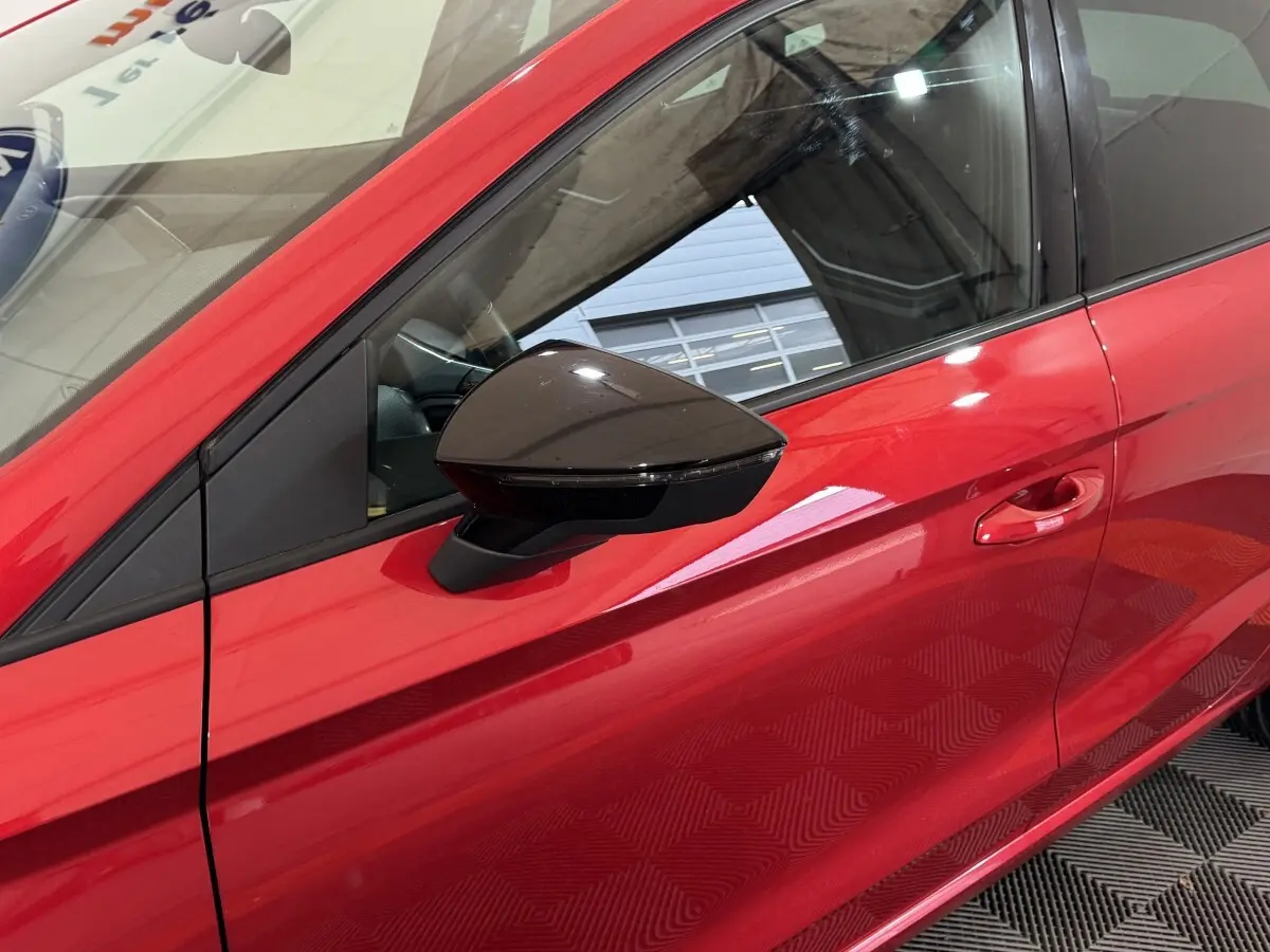 Vue rapprochée du côté gauche d'une SEAT IBIZA 1.0 TSI 110 FR rouge avec rétroviseur noir brillant.