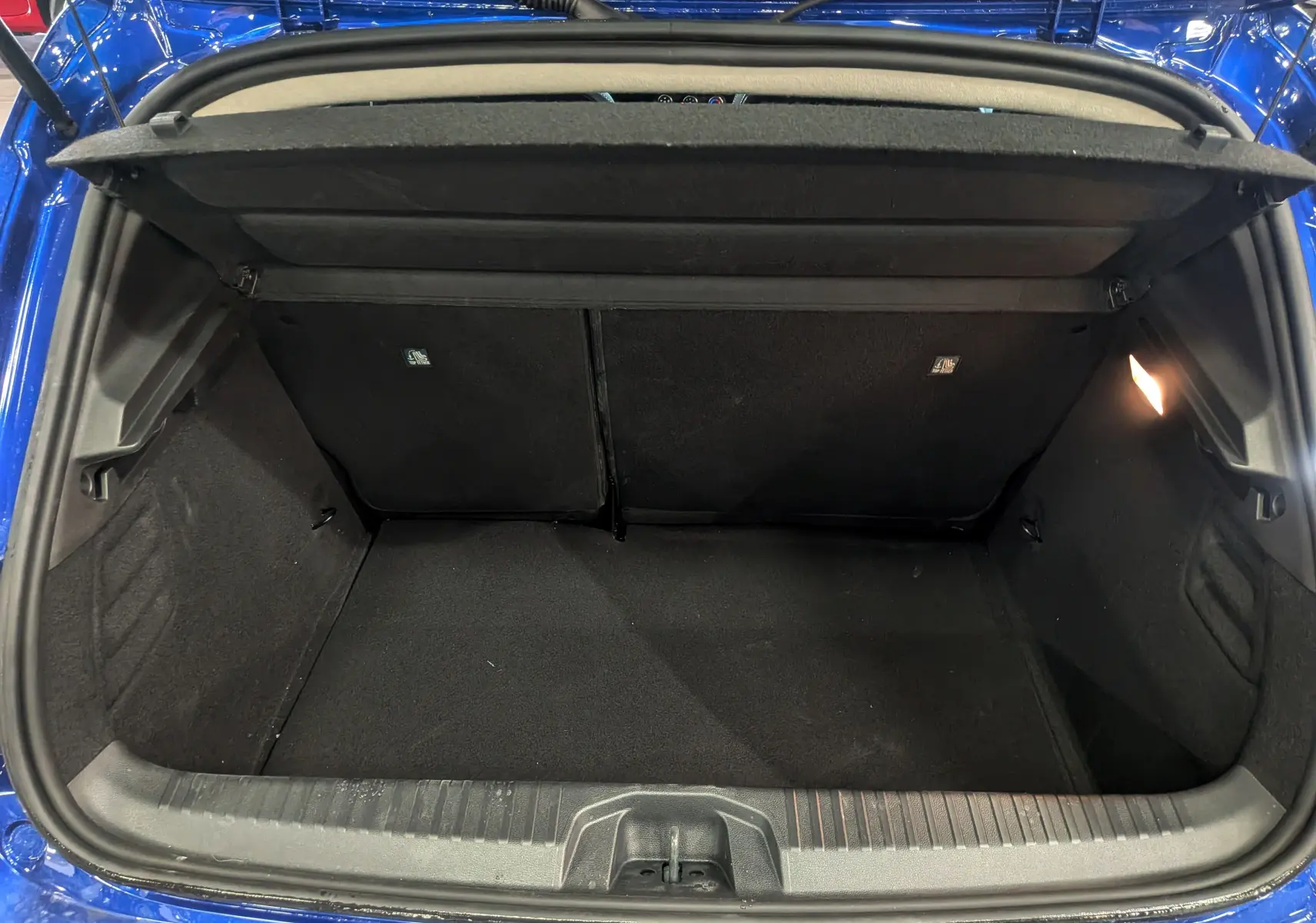 Coffre ouvert vu de l'arrière d'une Renault Clio V Bleu Iron, montrant l'espace de rangement et la lumière intérieure allumée.