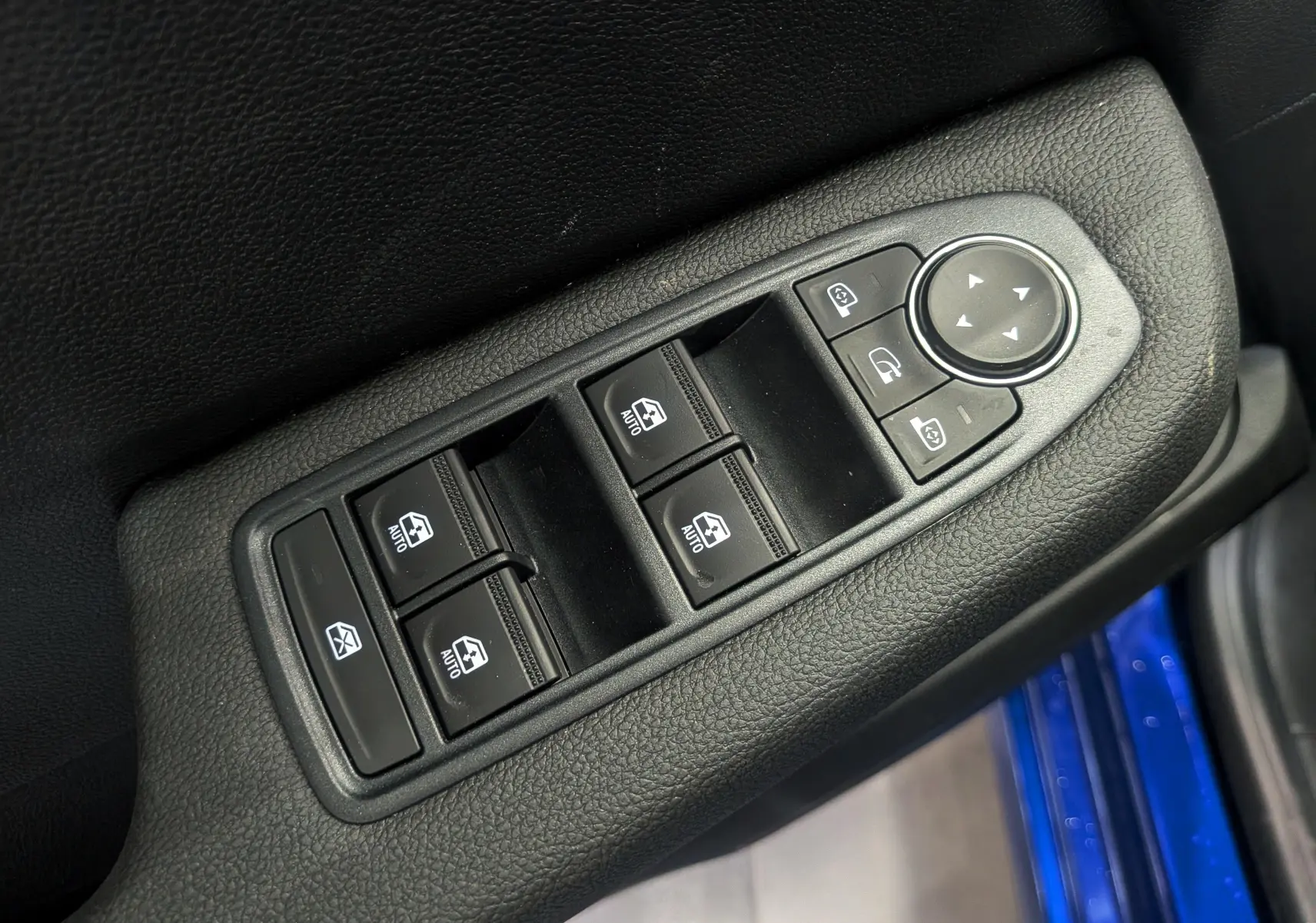 Gros plan sur les commandes des vitres électriques et des rétroviseurs sur la porte côté gauche d'une Renault Clio V Bleu Iron.