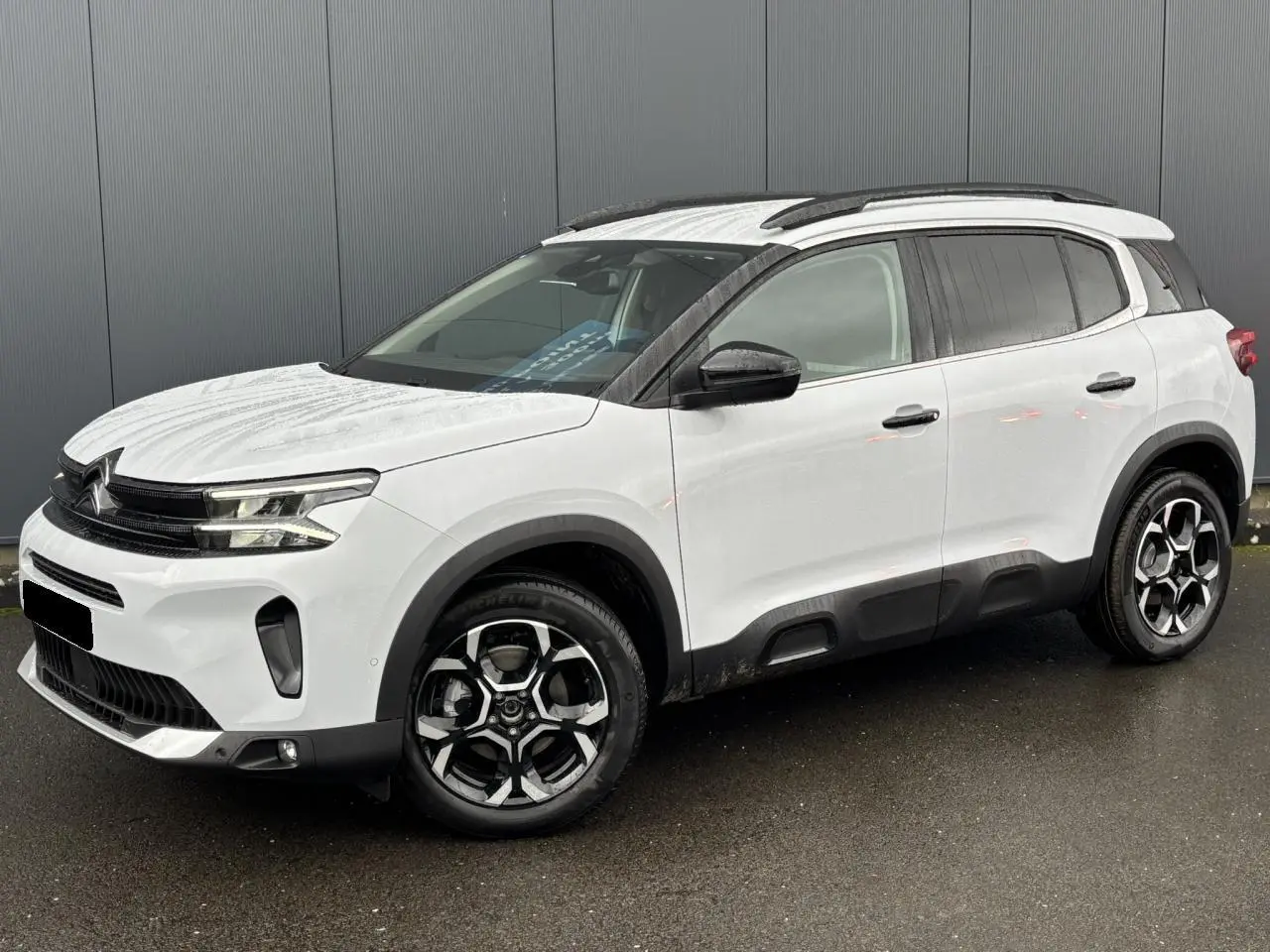 Vue 3/4 avant droite du Citroën C5 Aircross blanc Okénite avec jantes alliage bi-ton et barres de toit noires.