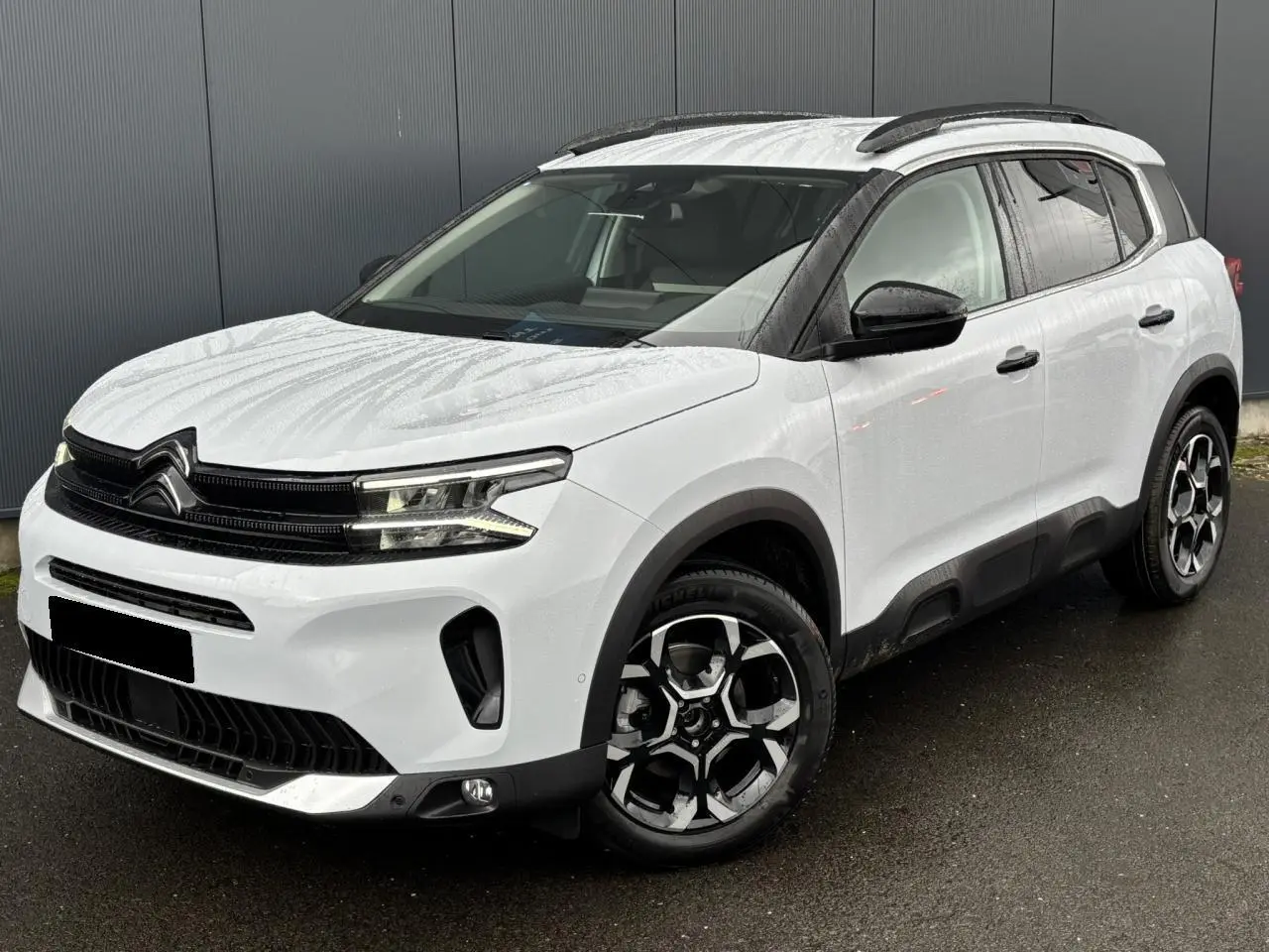 Vue 3/4 avant droit d'un Citroën C5 Aircross blanc Okénite avec jantes alliage bi-ton et barres de toit noires.