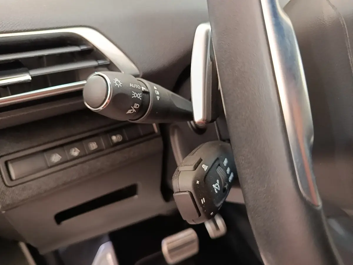Gros plan sur la commande des phares et volant en cuir noir du Peugeot 3008 hybride bleu, intérieur côté gauche.