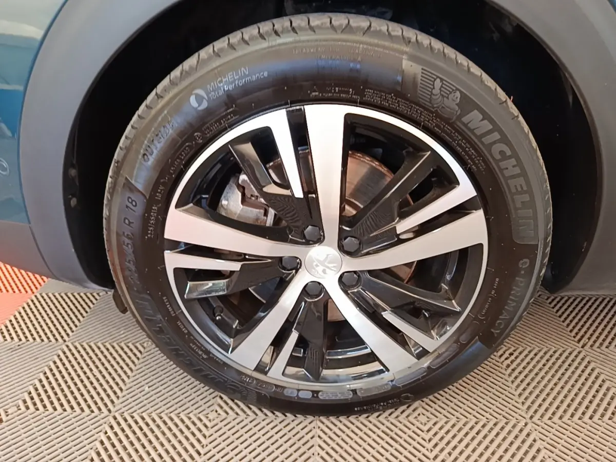 Gros plan sur la roue avant droite d’un Peugeot 3008 bleu 1.6 Hybrid 225 GT avec jante alliage bicolore.