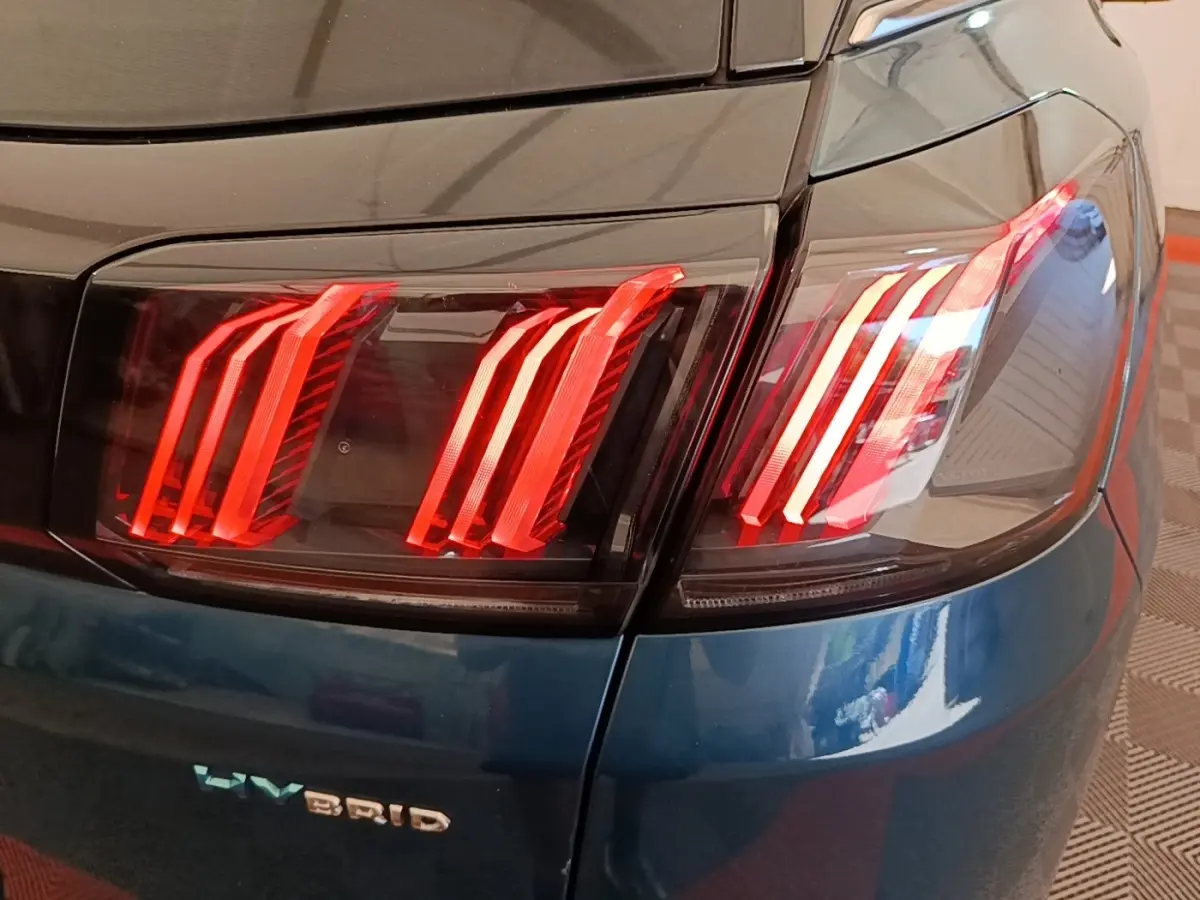Gros plan sur le feu arrière droit rouge du Peugeot 3008 hybride bleu, avec logo HYBRID visible sur la carrosserie.