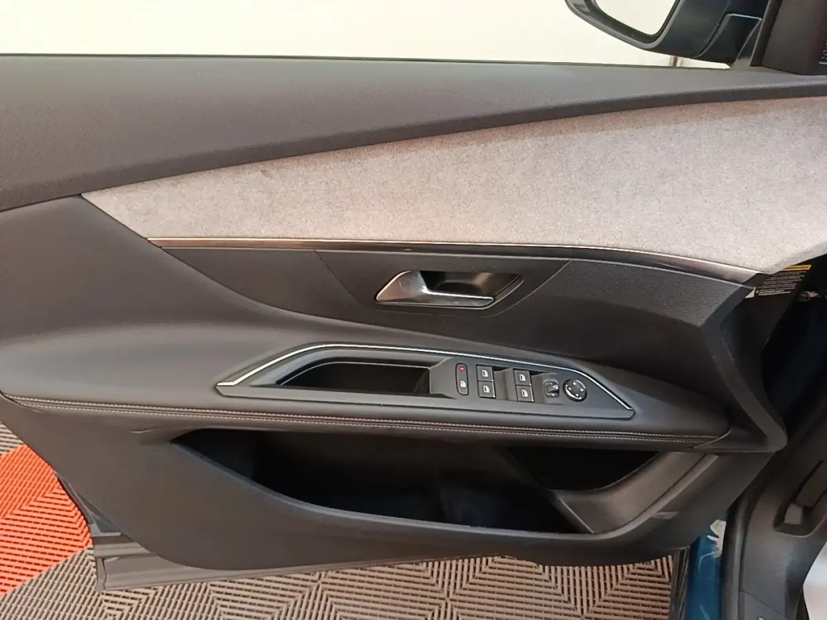 Vue intérieure côté gauche de la porte avant d'un Peugeot 3008 bleu avec commandes de vitres et poignée intégrée.