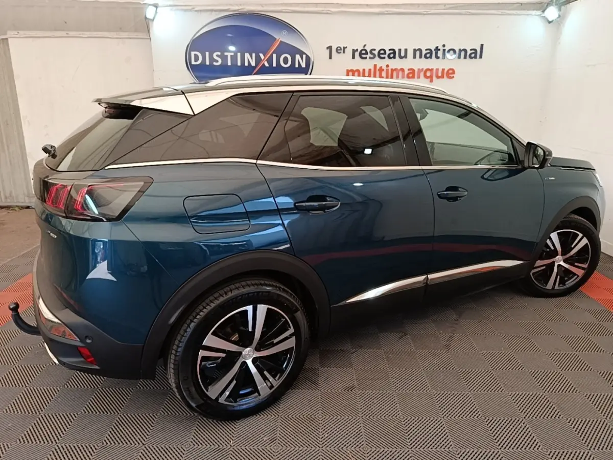 Vue 3/4 arrière droite du Peugeot 3008 hybride rechargeable bleu avec jantes alliage et toit blanc en intérieur showroom.