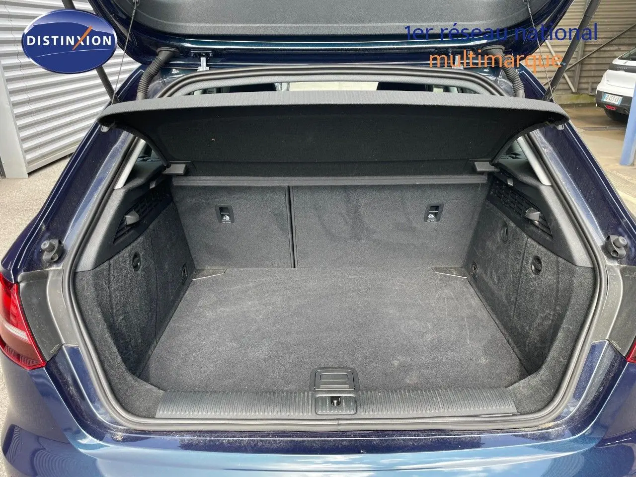 Coffre ouvert d'une Audi A3 Sportback bleu cosmos métal, vue arrière montrant l'espace de chargement vide et la plage arrière.