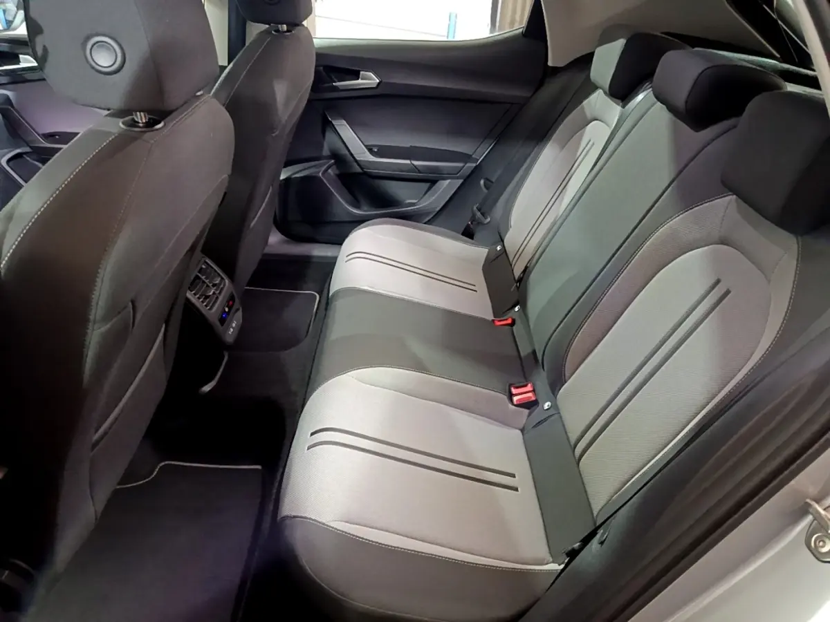 Vue intérieure arrière de la SEAT LEON 2023 montrant la banquette bicolore gris clair et foncé avec ceintures rouges.