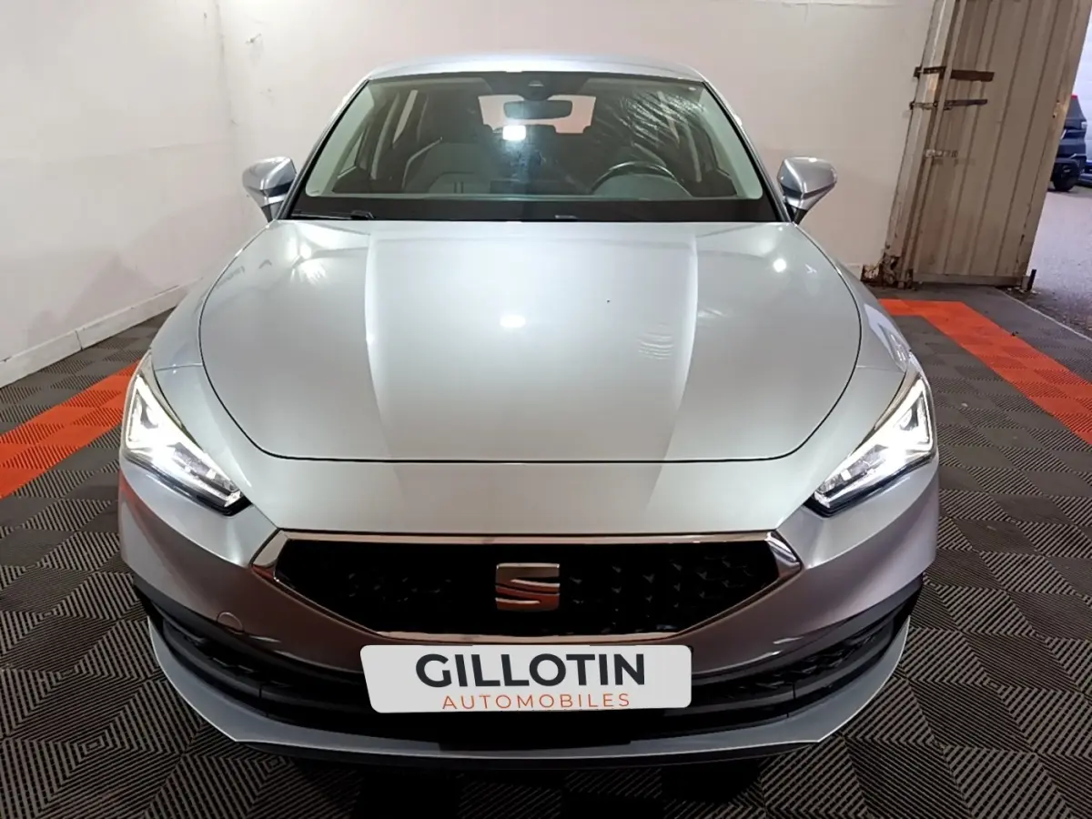 Vue frontale d'une SEAT Leon gris clair avec phares LED allumés et calandre noire hexagonale.