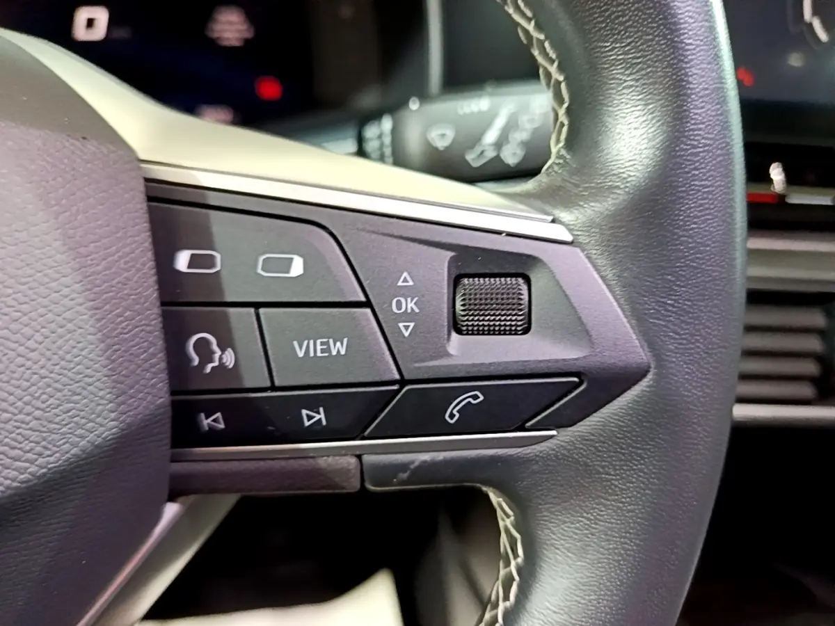 Gros plan sur les commandes gauche du volant cuir du SEAT LEON gris clair 2023 avec boutons multifonctions visibles.