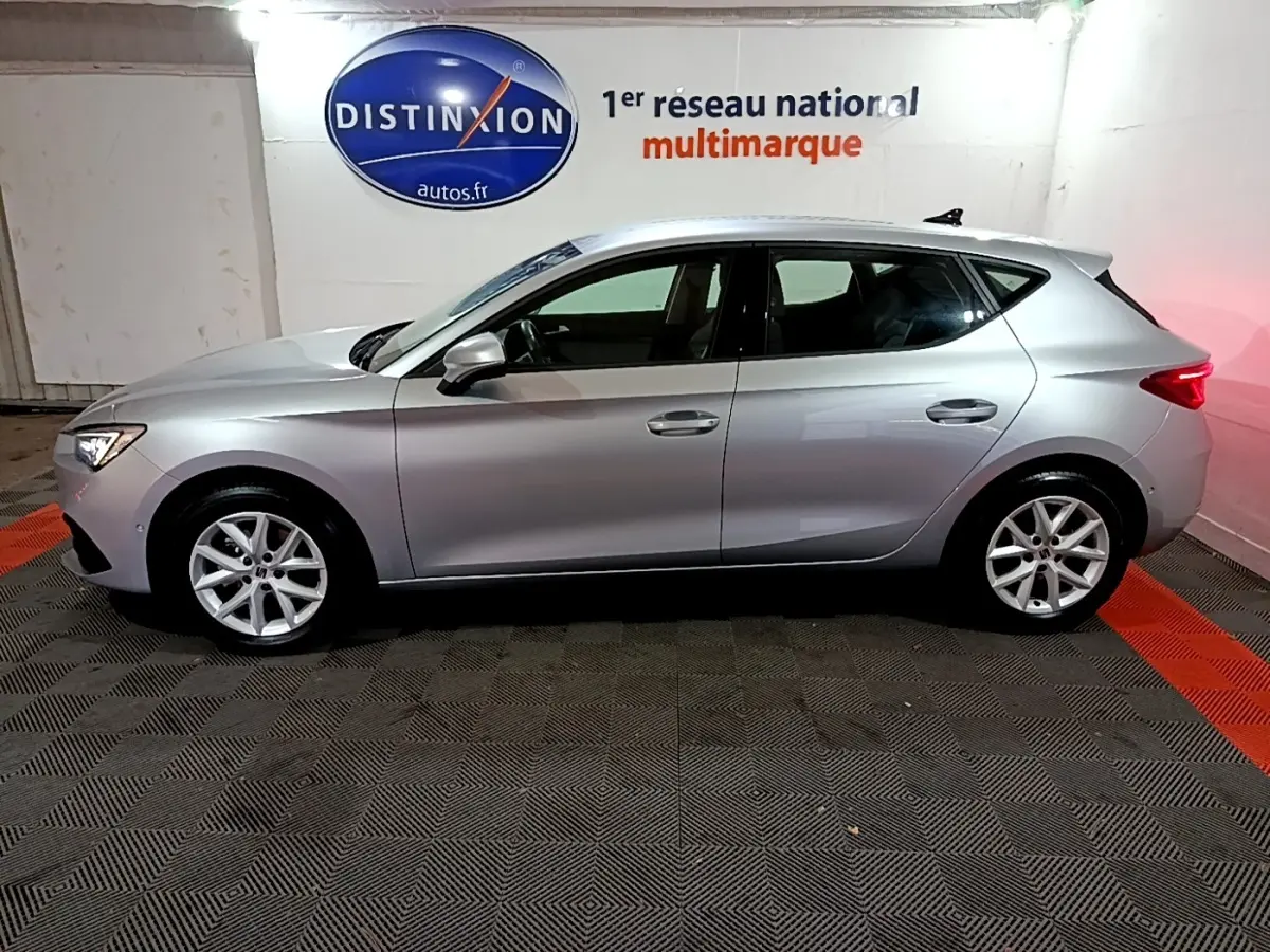 Profil côté gauche d'une SEAT LEON gris clair 2023 garée en intérieur avec jantes alliage et feux arrière allumés.