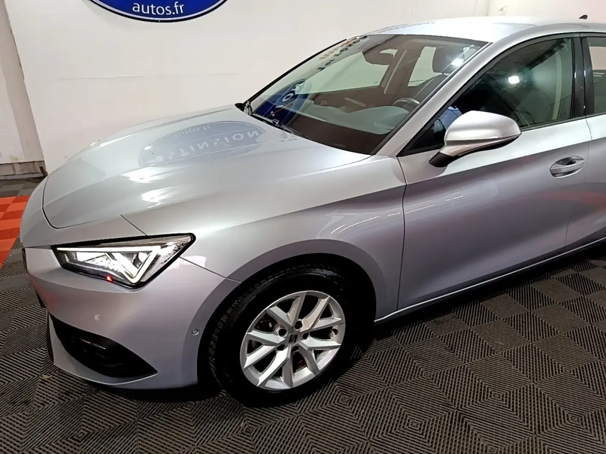 Vue 3/4 avant droit d'une SEAT Leon gris clair avec phares LED et jantes alliage en showroom.