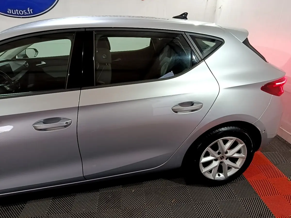 Vue latérale côté gauche d'une SEAT Leon gris clair 2023 avec jantes alliage et vitres teintées.