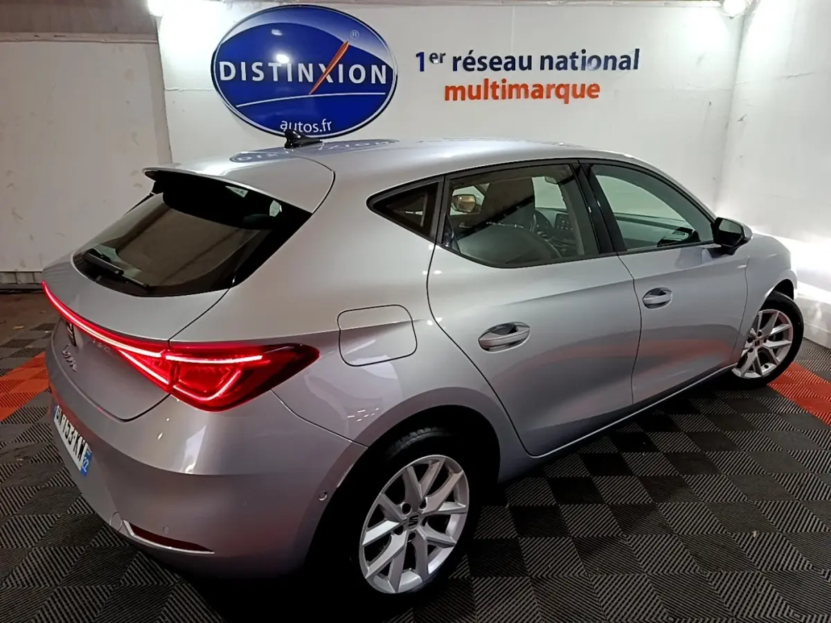 Vue 3/4 arrière droite d'une SEAT Leon gris clair 2023 avec feux LED et jantes alliage dans un showroom.