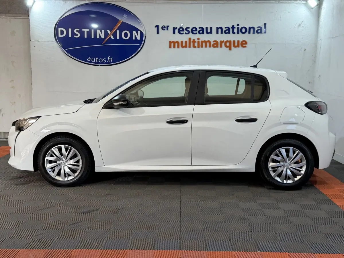 Vue de profil côté gauche d’une Peugeot 208 PureTech 75 S&S Like blanche, avec jantes alliage et antenne de toit.