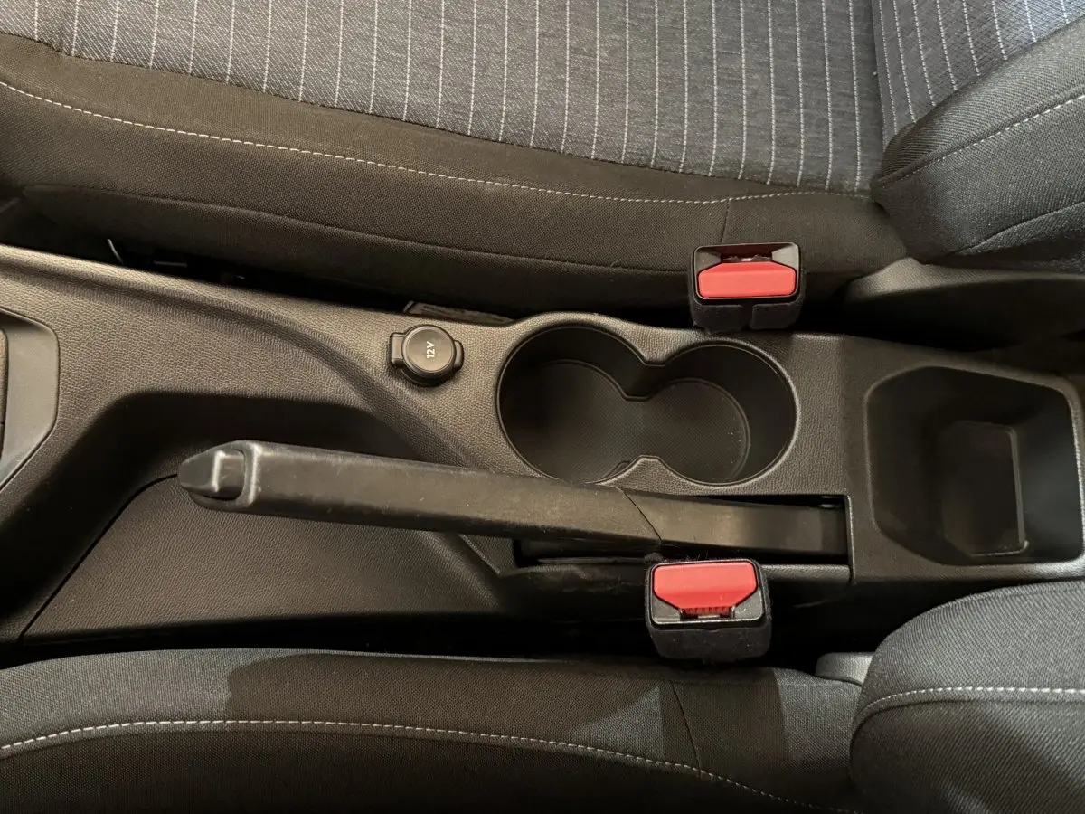Vue rapprochée de la console centrale noire de la Peugeot 208 PureTech 75 S&S Like avec frein à main et porte-gobelets.