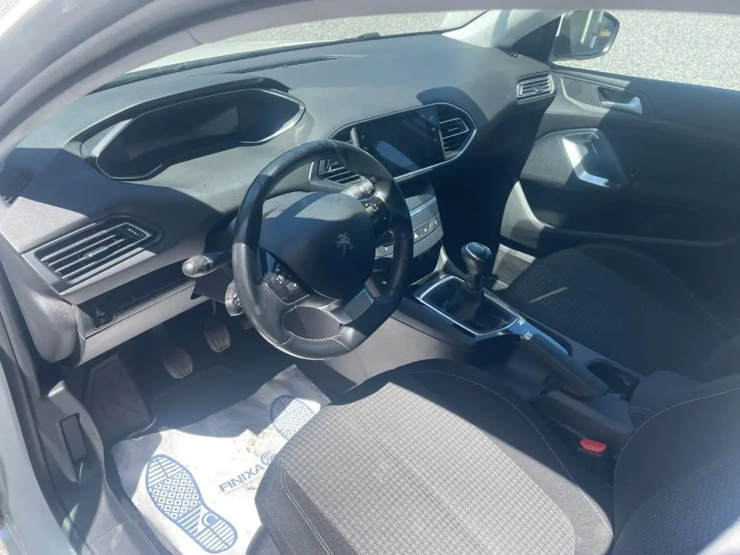 Vue intérieure côté conducteur du Peugeot 308 blanc, montrant le volant compact, la boîte manuelle et la console centrale moderne.