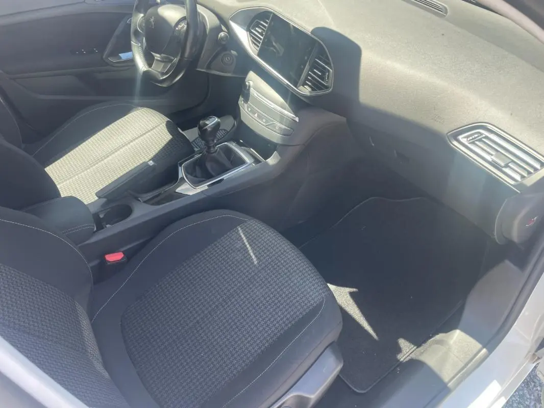 Intérieur avant droit de la Peugeot 308 blanche, montrant sièges tissu, tableau de bord et levier de vitesse manuel.
