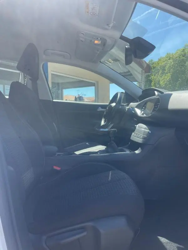 Vue intérieure côté conducteur de la Peugeot 308 blanche de 2020, montrant les sièges et la console centrale.