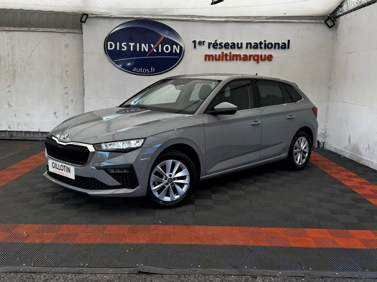 Vue 3/4 avant droite d'une Skoda Scala gris clair stationnée en intérieur avec jantes alliage et calandre noire distinctive.