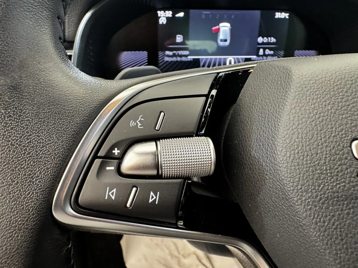 Gros plan sur la molette de commande et boutons multifonctions côté gauche du volant en cuir noir d'une Skoda Scala gris clair.
