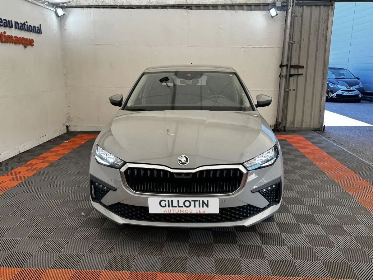 Vue frontale d'une Skoda Scala gris clair avec calandre noire et phares LED allumés en intérieur showroom.