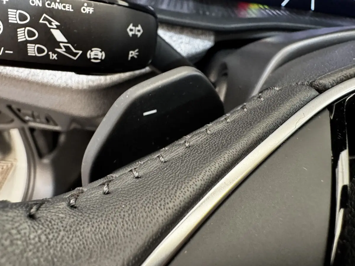 Gros plan sur la palette de changement de vitesse derrière le volant cuir du Skoda Scala gris clair, détails des commandes visibles.