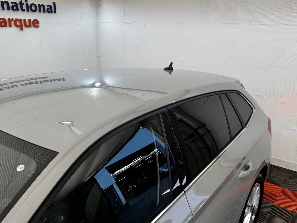 Vue 3/4 arrière droite d'une Skoda Scala gris clair avec vitres teintées et jantes argentées dans un showroom.
