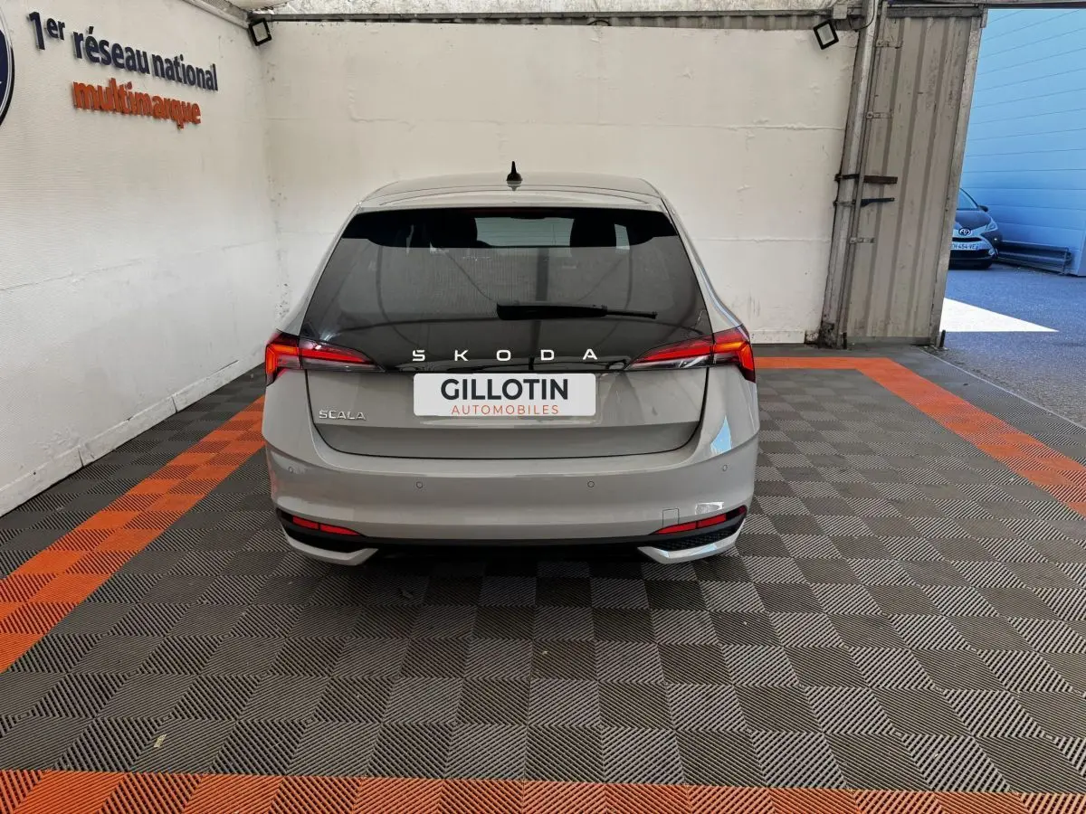 Vue arrière d'une Skoda Scala gris clair 2025 dans un garage avec éclairage naturel à droite.