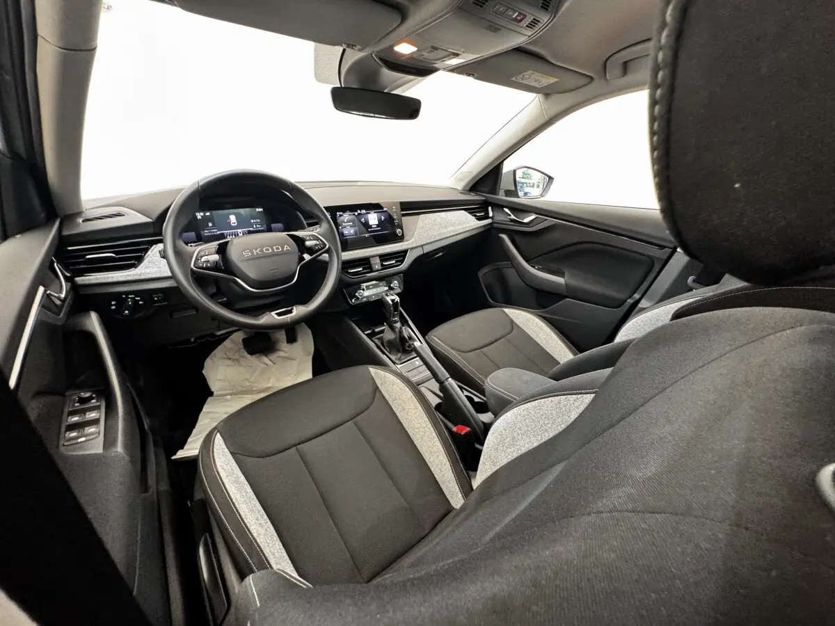 Vue intérieure avant droite de la Skoda Scala 2025, sièges bicolores gris clair et noir, tableau de bord moderne avec écran tactile.