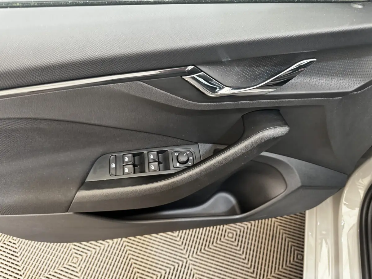Vue rapprochée de la porte avant gauche de la Skoda Scala gris clair, avec commandes des vitres et poignée noire.