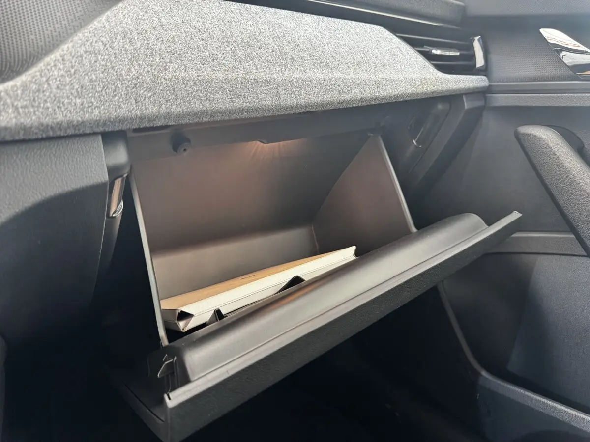 Gros plan sur la boîte à gants ouverte côté passager du Skoda Scala gris clair, montrant l'intérieur et un manuel.