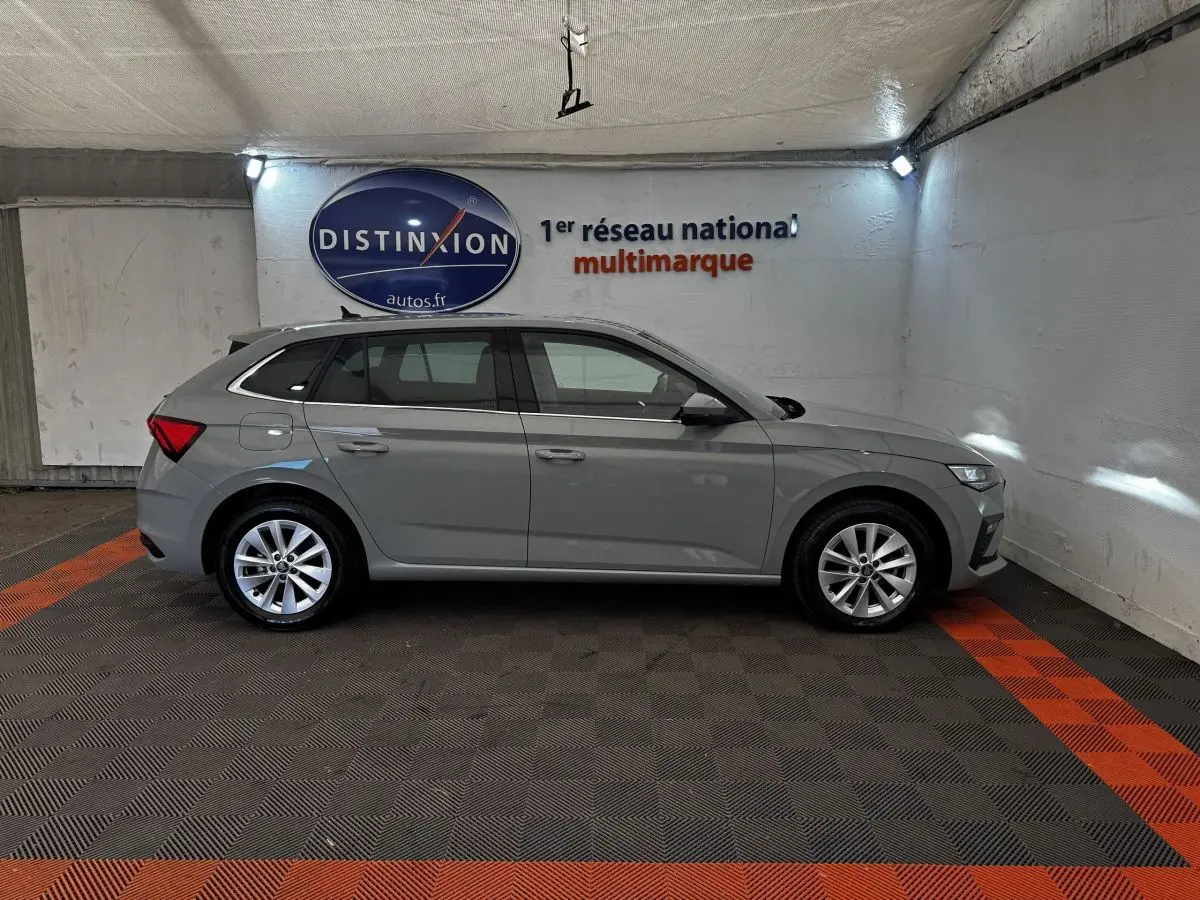 Vue de profil côté gauche d'une Skoda Scala gris clair 2025 stationnée en intérieur avec jantes alliage et feux arrière distinctifs.