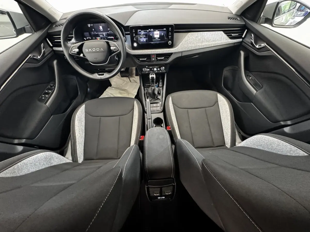 Vue intérieure avant de la Skoda Scala 2025, tableau de bord moderne avec écran tactile et sièges bicolores gris et noir.